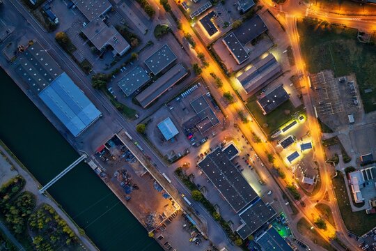 Aerial view of the industrial district in Mulhouse, illuminated by streetlights at dusk, featuring warehouses, a canal, and road networks in Mulhouse, Grand Est, France.