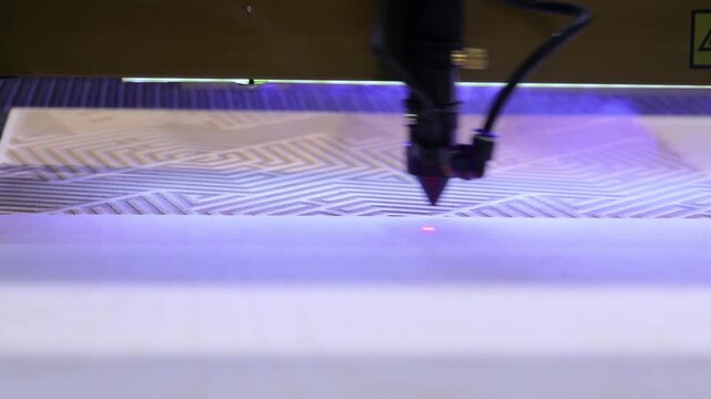 Laser cutter machine engraving intricate geometric patterns onto wood surface in high precision manufacturing process.