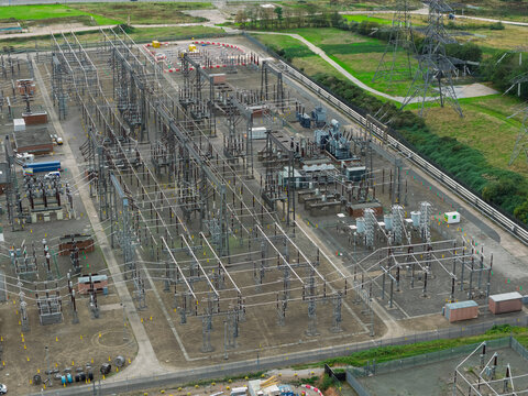 Aerial view of an electrical substation with metal structures, transformers, and power lines set against a grassy landscape in United Kingdom.