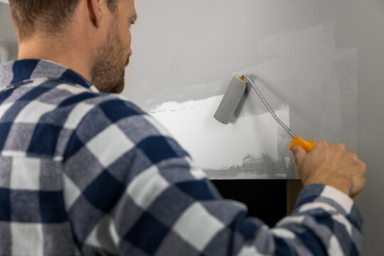 Handyman painting plaster patch with paint roller after wall repair
