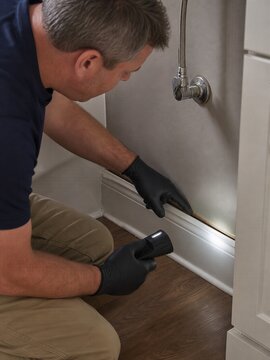 Technician checks swollen baseboard after bathroom water leak damage
