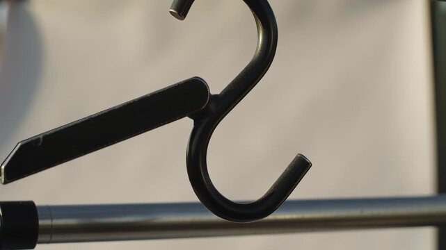 Swaying black S-shaped metal hook rotating on outdoor steel rod in breeze, with clip and clamp