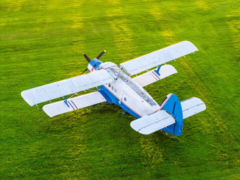 Aerial view of an Antonov An-2 biplane parked on a lush green field during golden hour in Latvia.