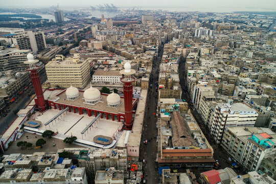 Aerial view of the Memon Masjid with its distinctive red minarets and white domes, surrounded by the dense urban landscape and bustling streets of Karachi, Sindh, Pakistan.