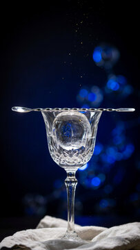 Crystal cocktail glass with an ice sphere and metal bar strainer set against a dark blue bokeh background cocktail strainer beverage refreshment nightlife mixology transparent reflective