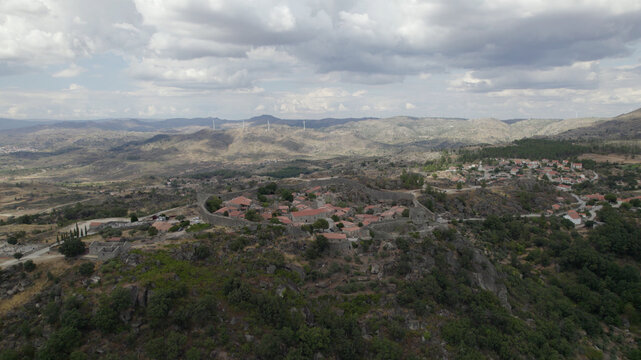 Aerial view of the historic village of Sortelha with stone walls and terracotta rooftops surrounded by rocky hills and a cloudy sky in Sortelha, Distrito da Guarda, Portugal.