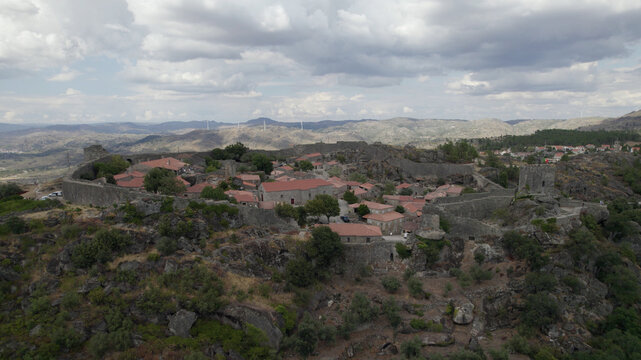 Aerial view of the historic fortified village of Sortelha with stone houses, red-tiled roofs, and medieval castle walls set amidst a rocky landscape in Sortelha, Distrito da Guarda, Portugal.