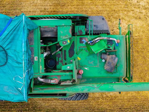 Aerial view of a green combine harvester broken down in a harvested field with an open engine compartment, tools, and a blue tarp in Jaunberze Parish, Dobele Municipality, Latvia.