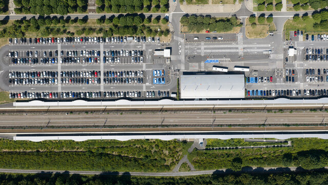 Aerial view of TGV Haute Picardie station featuring an extensive parking lot, parallel railway tracks, and surrounding green landscape in Estrees-Deniecourt, Hauts-de-France, France.