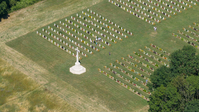 Aerial view of the Thiepval Memorial cemetery with rows of white headstones, a central stone cross, and visitors walking on the grass in Authuille, Hauts-de-France, France.