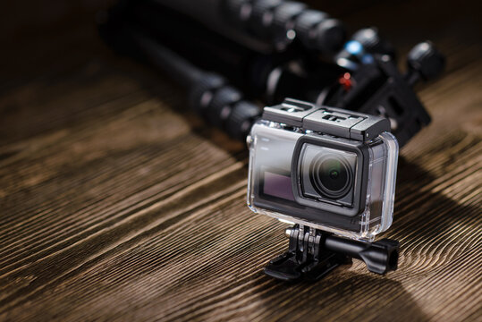 Action camera in waterproof case on wooden table with tripod in background.