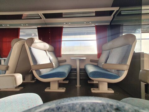 Empty Train Interior With Paired Seats and Window Table, Sunlit Commuter Carriage With Red Curtains