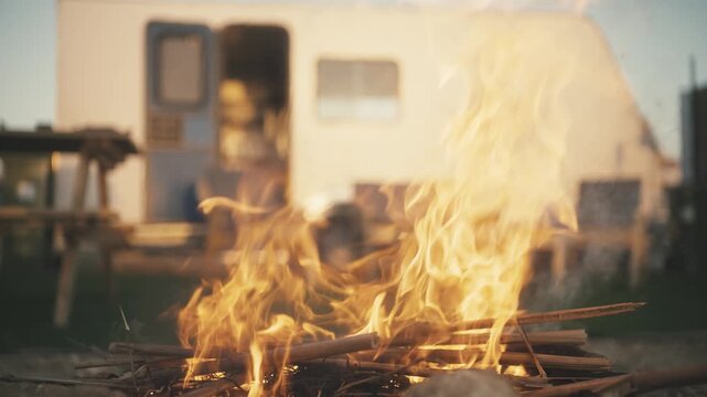 Small campfire burning on rocks outdoors with a camper van and outdoor furniture in the background