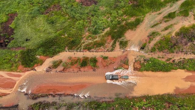 Aerial view of a 4x4 vehicle with a trailer navigating through a flooded rural dirt road during heavy rainfall, surrounded by lush vegetation, Louis Trichardt, Limpopo, South Africa.