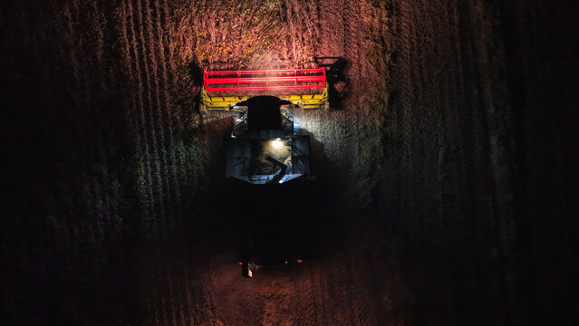 Aerial view of a combine harvester working in a field at night, illuminated by its bright headlights while harvesting crops in Crepaja, Vojvodina, Serbia.