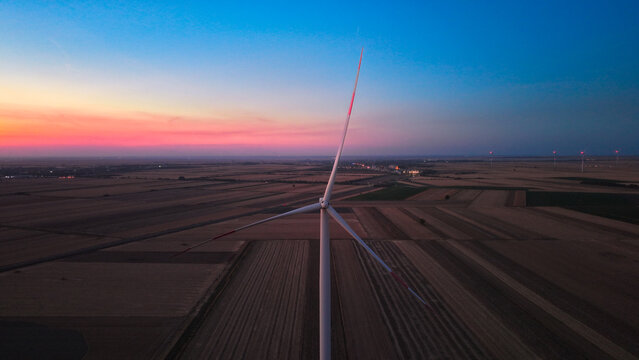 Aerial view of a wind turbine silhouetted against a vibrant sunset over agricultural fields in Kovacica, Vojvodina, Serbia.