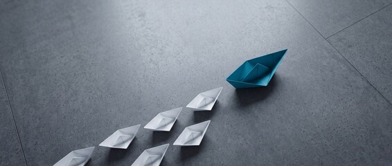 Fototapeta premium Leading the Way Concept: A Single Blue Paper Boat Navigating Forward Followed by a Group of White Paper Boats on a Gray Stone Floor, Representing Leadership, Teamwork, and Business Strategy.