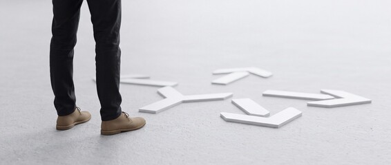 Fototapeta premium Close up of businessman legs standing at a crossroads of white directional arrows on a concrete floor, conceptualizing strategic decision making, career path choices, and perspective shift.