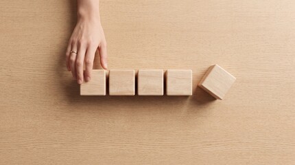 Fototapeta premium Overhead view of a hand arranging a row of blank wooden blocks on a light wooden surface, symbolizing business strategy, planning, organization, structure, and professional growth concepts.