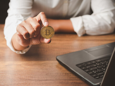 Businessperson holding cryptocurrency coin beside laptop  