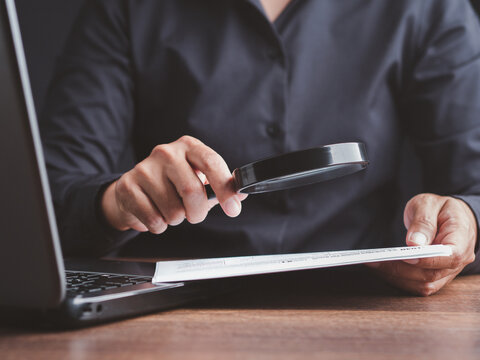 Person inspecting document with magnifying glass at desk  