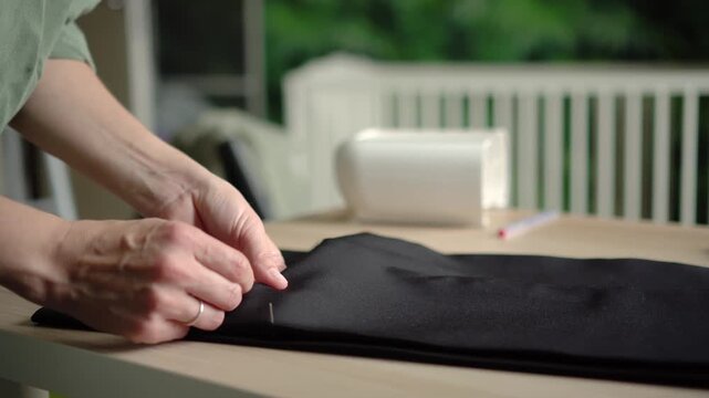 A woman seamstress and artisan manipulate black fabric on a table, stitching with deliberate precision. This mindful craftswoman creates a serene atmosphere while working in her quiet studio.