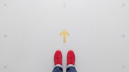 Fototapeta premium Top view of a person wearing red sneakers standing in front of a yellow forward arrow on a gray floor, representing concepts of choice, direction, decision making, and career path planning.