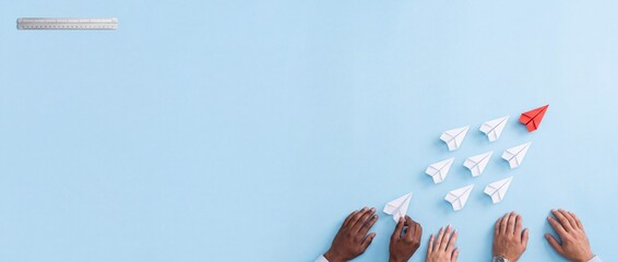 Fototapeta premium Strategic business leadership and teamwork concept featuring a red paper plane leading white ones on a wide blue background with diverse hands and a ruler for measurement and planning