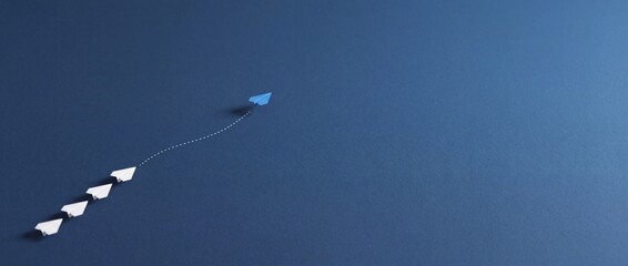 Fototapeta premium Blue Paper Airplane Changing Direction and Leading White Ones on Navy Blue Background, Concept of Leadership, Innovation, Business Strategy and Thinking Outside the Box with Wide Copy Space