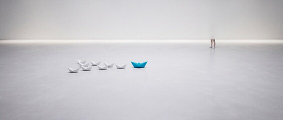 Fototapeta premium Wide conceptual shot of a blue origami paper boat leading a group of white paper boats on a minimalist white surface representing leadership, individuality, and business strategy concepts.