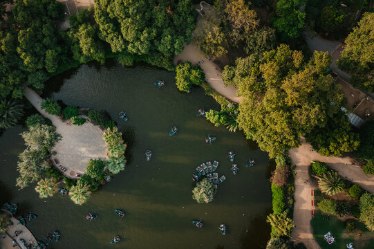 Aerial view of the lake in Ciutadella Park with people rowing small boats surrounded by lush green trees and walking paths in Barcelona, Catalonia, Spain.