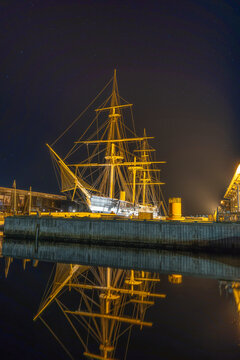 Illuminated historic frigate Jylland reflecting in still harbor water under a starry night sky