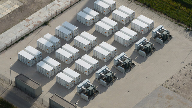 Aerial view of a battery energy storage system with rows of white shipping containers and electrical transformers on a paved site in Dronten, Flevoland, Netherlands.