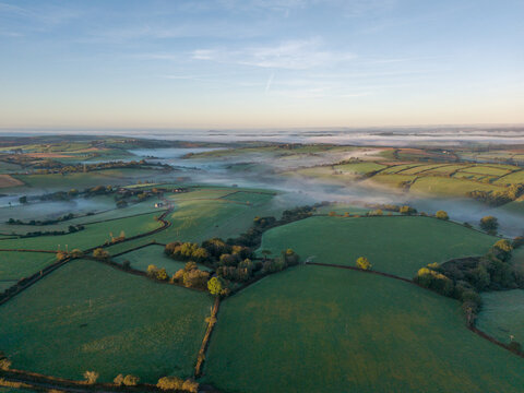 Aerial view of the rural countryside landscape in Looe featuring green fields, hedgerows, and morning mist under the soft golden hour light, Looe, England, United Kingdom.