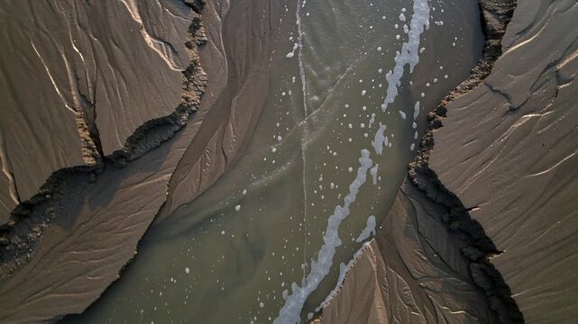 Ebb tide pulling tidal channel carrying foam bubbles while drone moving over rippled sandbanks