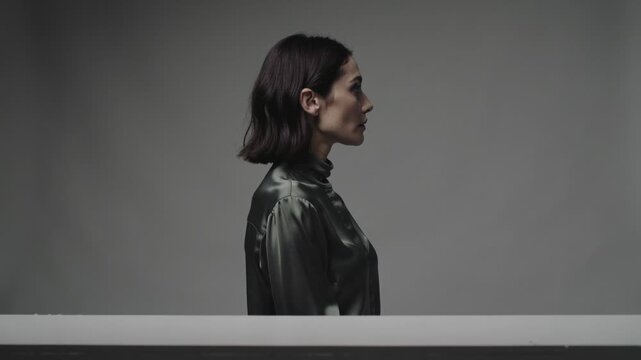 On cue walking model wearing dark satin blouse, moving across studio grey backdrop with low ledge