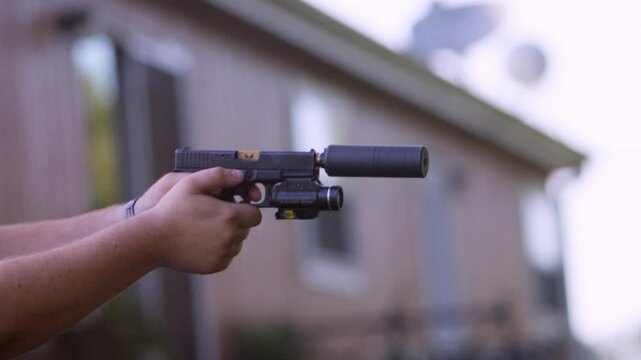 Close-up side view of a shooter firing a suppressed 1911-style pistol outdoors, capturing recoil, slide movement, and a steady two-handed grip in cinematic slow motion.