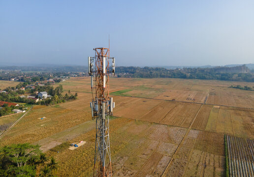 Aerial view of a telecommunications tower standing amidst vast agricultural fields and rural landscape in Patikraja, Central Java, Indonesia.
