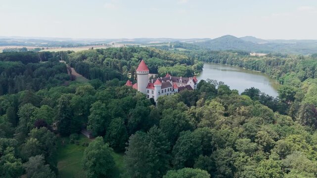 Drone makes a half-circle around Konopi&scaron;tě with the lake constantly in view, revealing the forested hill and distinctive tower rising above the surrounding trees.