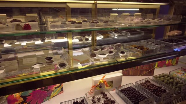Rows of packaged candies and sweet snacks are displayed along retail shelves inside a brightly lit candy shop.