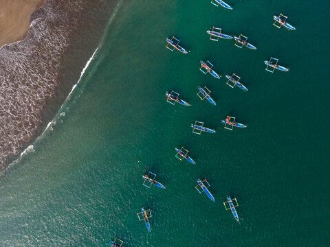 Aerial view of traditional outrigger fishing boats floating on the turquoise sea near the sandy coastline in Cilacap, Central Java, Indonesia.