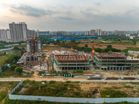 Aerial view of a large construction site with multiple cranes and partially completed high-rise buildings, surrounded by urban development in Gurugram, Haryana, India.