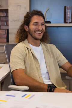 Adult man sitting at modern office desk leaning back smiling with wristwatch and printed charts