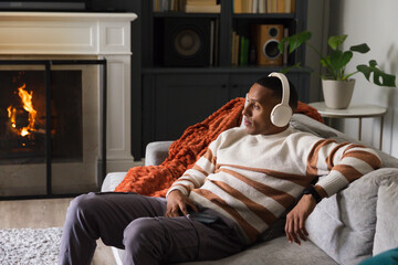Fototapeta premium African American man reclining on light gray sofa in living room, wearing headphones