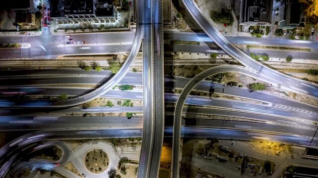 Aerial overhead time lapse view of a illuminated highway with interchange, crossroads and car traffic as a urban transport concept