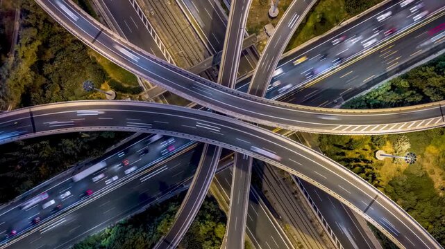 Aerial overhead time lapse view of a illuminated highway interchange with crossroads, curves and heavy car traffic as a urban transport concept