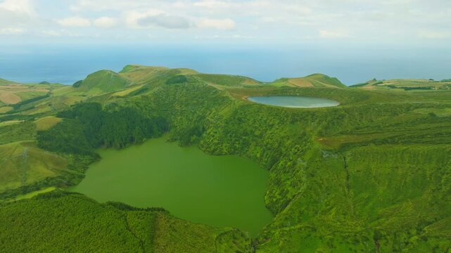 Aerial view of the spectacular volcanic crater lakes Lagoa Rasa and Lagoa Funda on Flores Island, Azores, Portugal. High viewpoint over lush green calderas with the Atlantic Ocean on the horizon
