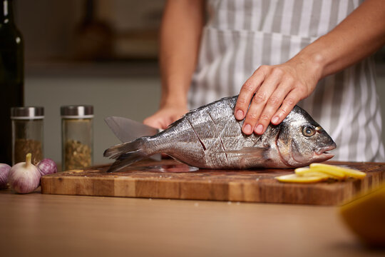 Woman preparing fresh sea bream for cooking dinner