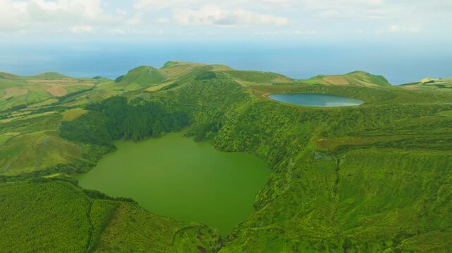 Aerial view of the spectacular volcanic crater lakes Lagoa Rasa and Lagoa Funda on Flores Island, Azores, Portugal. High viewpoint over lush green calderas with the Atlantic Ocean on the horizon