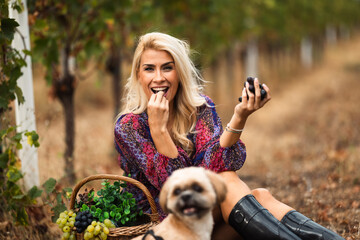 Fototapeta premium Smiling woman enjoying grapes in vineyard with dog beside her